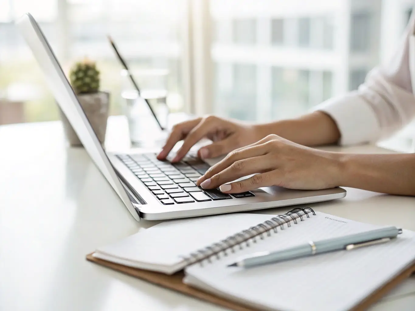 A close-up shot of a person's hands typing on a laptop, with a cup of coffee and a notebook nearby, symbolizing creative copywriting and content creation.